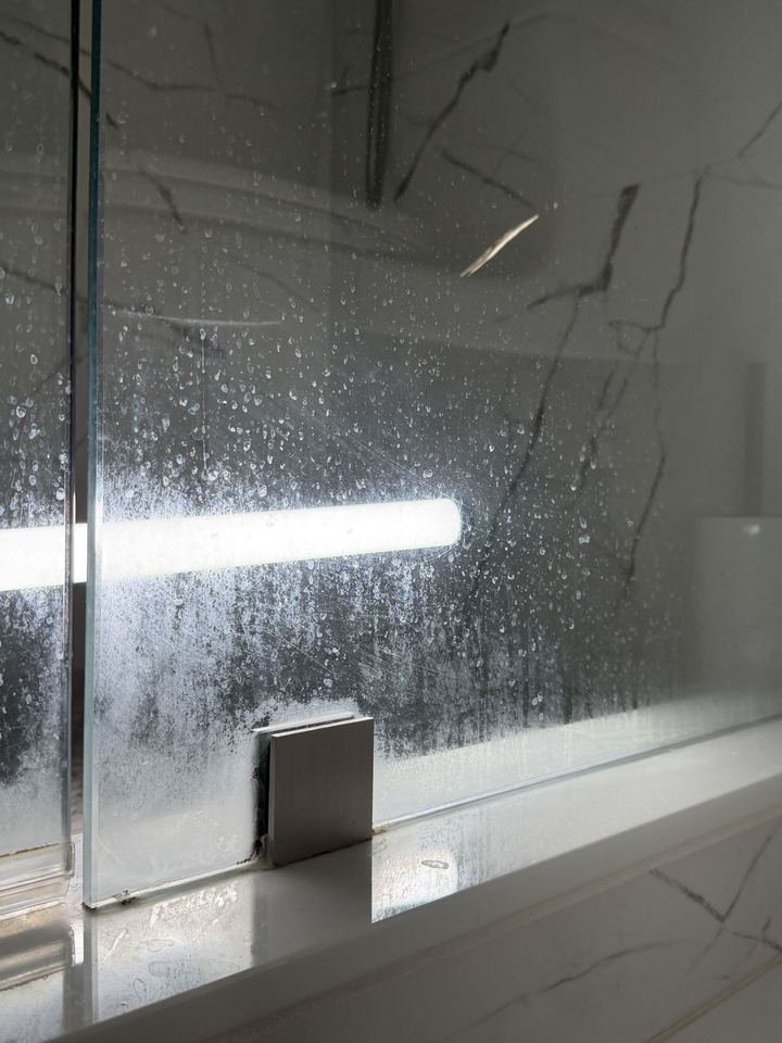Glass shower door covered in white hard water spots before cleaning